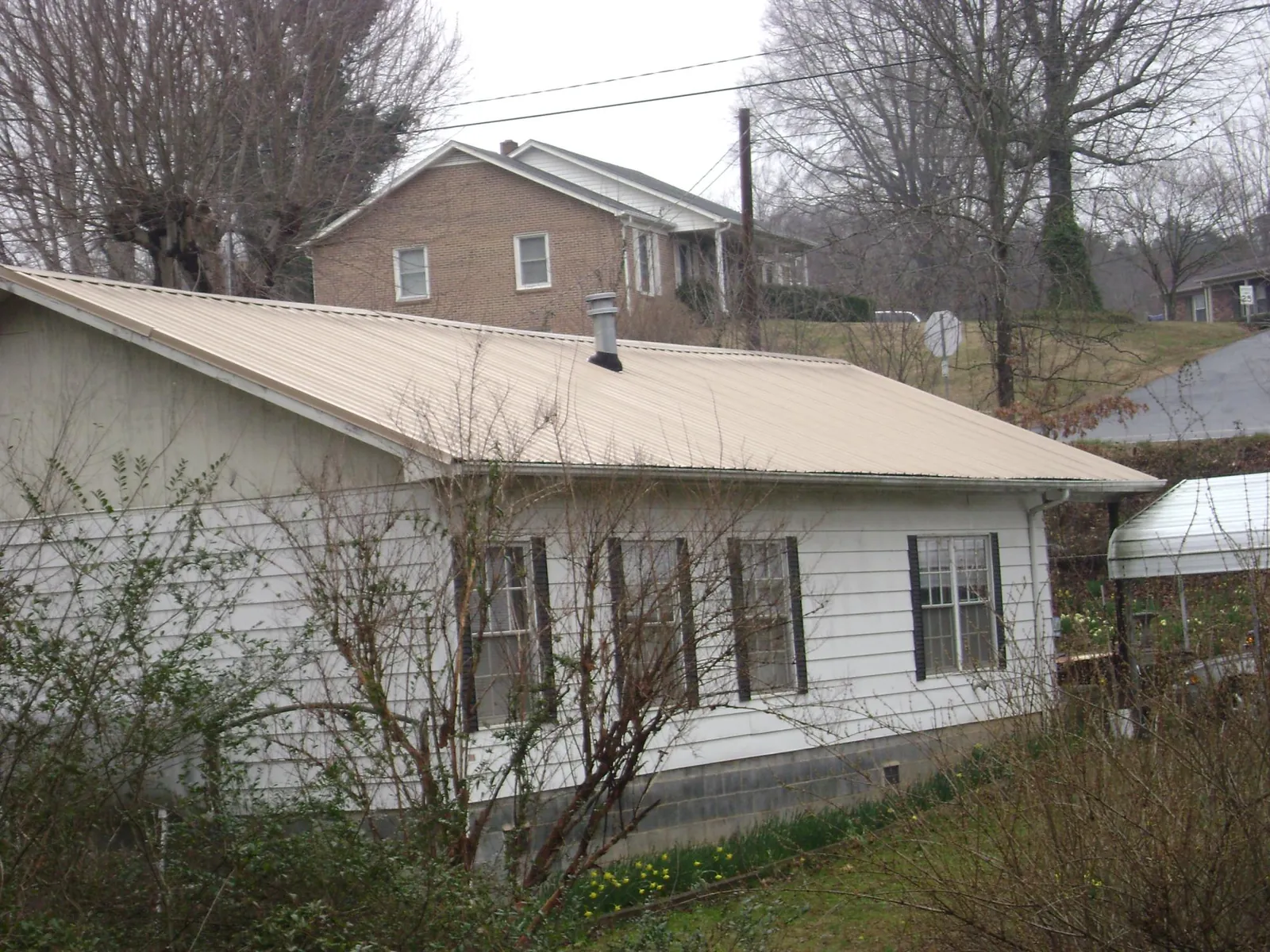 Tan metal roof on a white sided house set into a hillside — Commercial Roofing by Roofing Brothers in Taylorsville